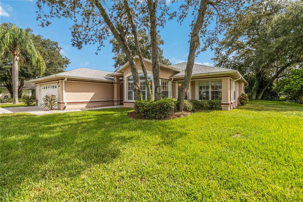 A single-story tan house with a two-car garage and large trees in the front yard — 2911 ELBERT WAY, KISSIMMEE, FL
