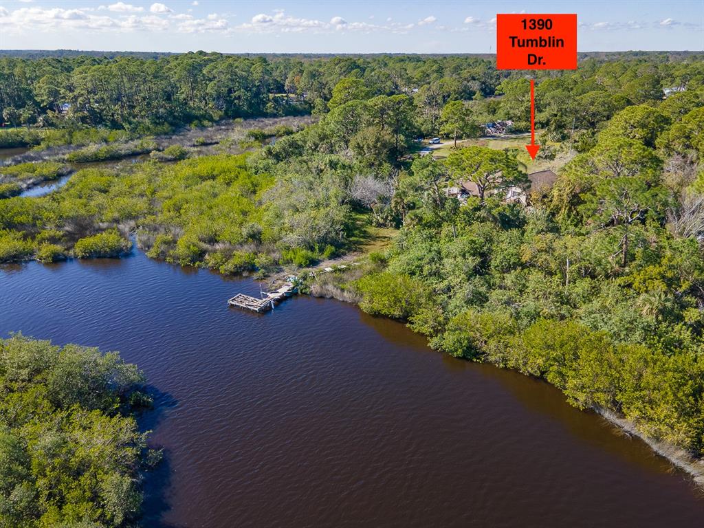 An aerial view shows a house nestled in a wooded area beside a small dock — 1390 TUMBLIN DRIVE, NEW SMYRNA BEACH, FL
