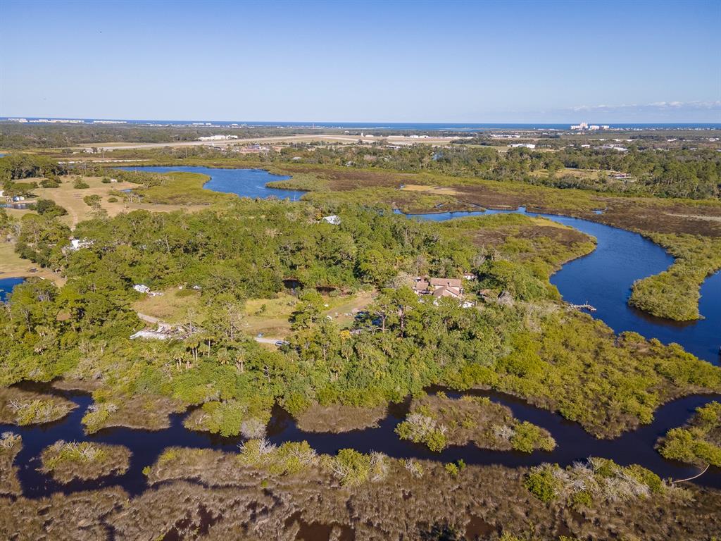 An aerial view shows a house surrounded by dense trees, marshland, and winding waterways — 1390 TUMBLIN DRIVE, NEW SMYRNA BEACH, FL