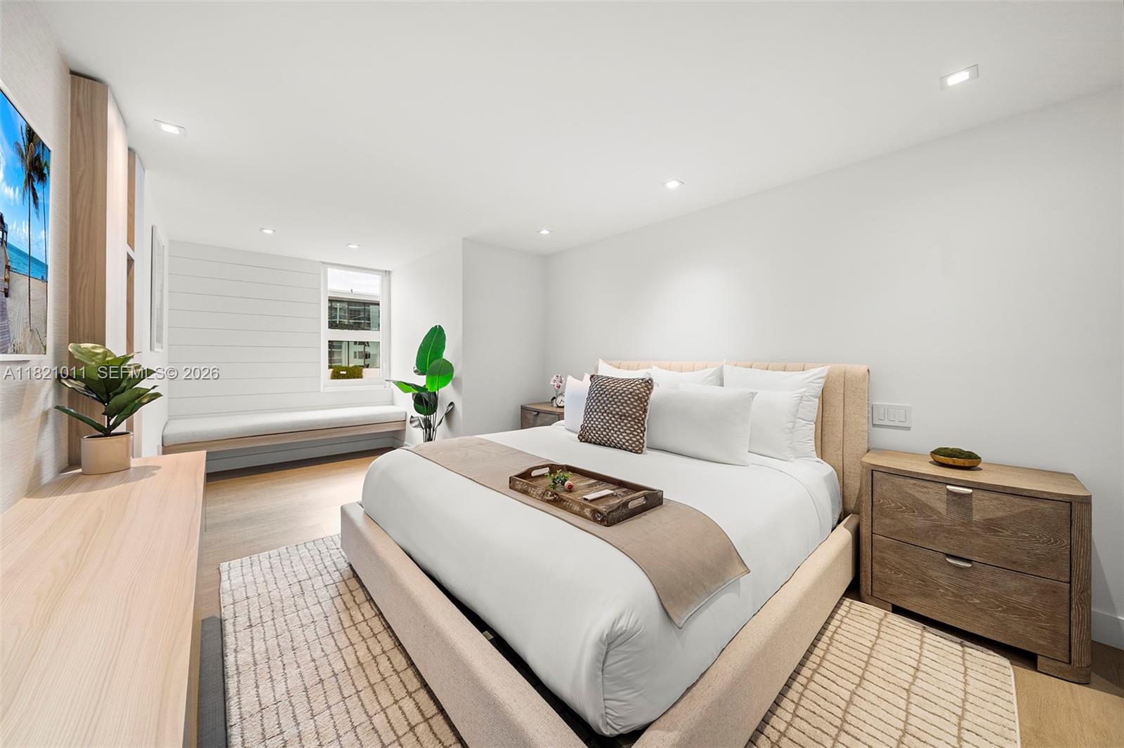 A modern bedroom features a beige upholstered bed, wood nightstands, and a built-in window seat — 2301 Collins Ave # 630, Miami Beach FL 33139, MIAMI BEACH, FL