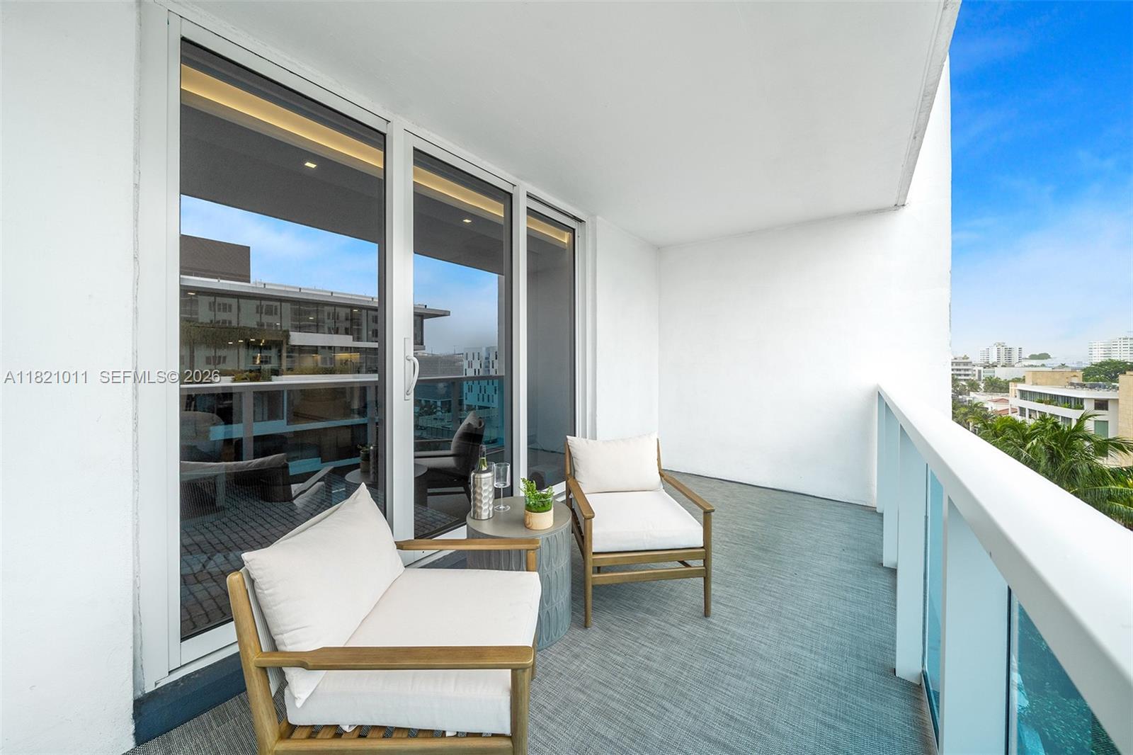 A balcony features two wooden chairs with white cushions and a small round table — 2301 Collins Ave # 630, Miami Beach FL 33139, MIAMI BEACH, FL