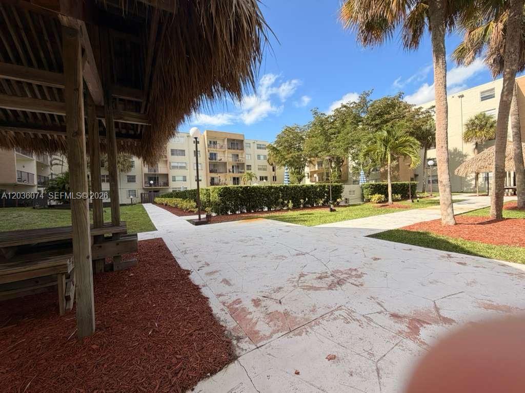 An outdoor patio area features a thatched-roof gazebo, paved walkways, and surrounding apartment buildings — 14250 SW 62nd St # 310, Miami FL 33183, MIAMI, FL