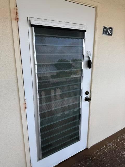 A white exterior door with a jalousie window insert and a lockbox, labeled number 76 — 76 Markham D, Deerfield Beach FL 33442, DEERFIELD BEACH, FL
