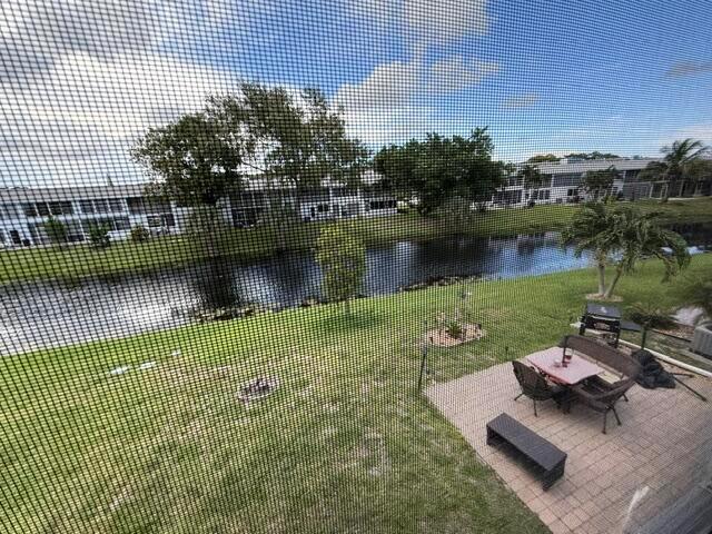 A view from a screened window overlooking a backyard patio, lawn, and a small canal — 76 Markham D, Deerfield Beach FL 33442, DEERFIELD BEACH, FL