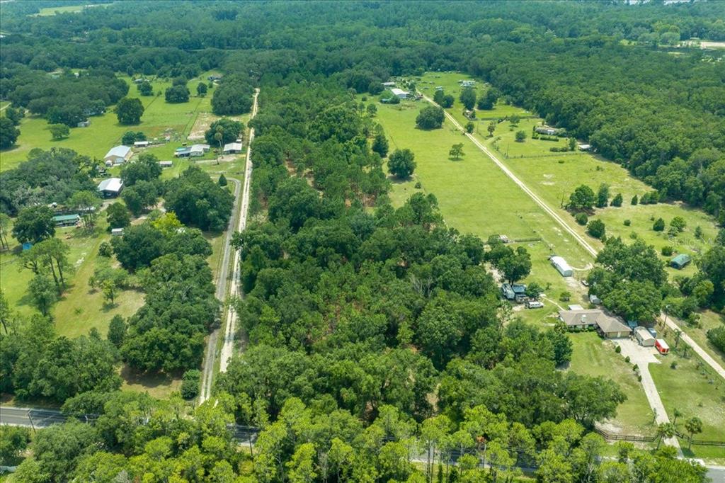 An aerial view shows a rural landscape with wooded areas, open pastures, and several houses — TBD SE 95TH ST RD, OCKLAWAHA, FL