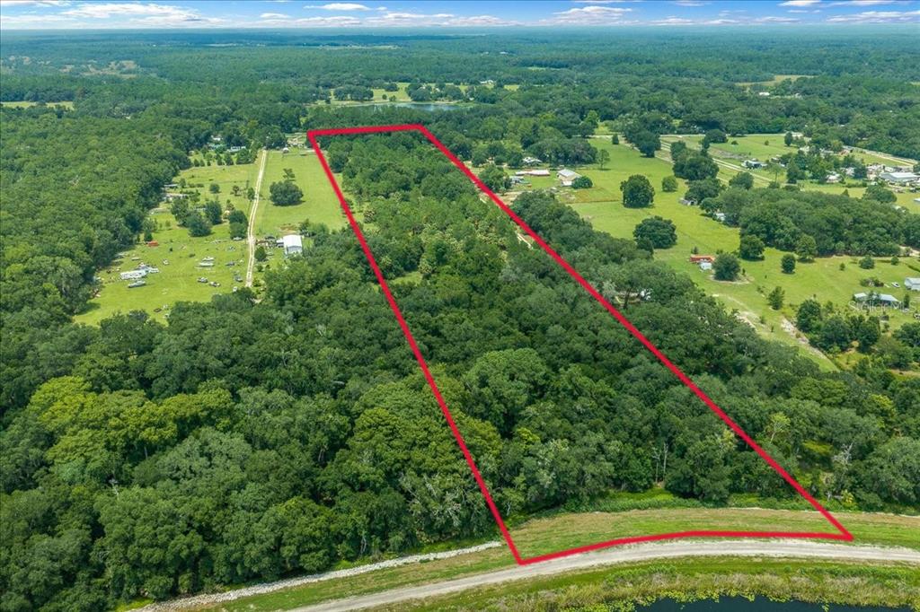 An aerial view shows a rectangular, tree-covered plot of land outlined in red near water — TBD SE 95TH ST RD, OCKLAWAHA, FL