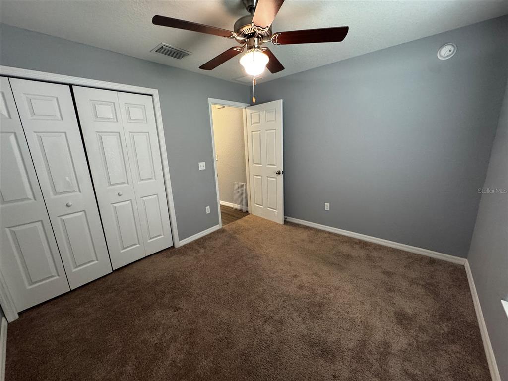 A bedroom features gray walls, brown carpeting, a ceiling fan, and white paneled doors — 13705 SE 54TH COURT, SUMMERFIELD, FL