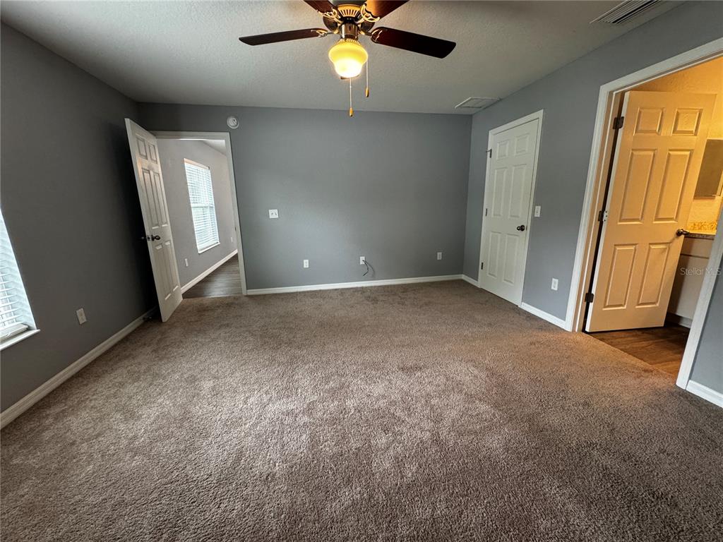 A bedroom with gray walls, carpeted flooring, a ceiling fan, and two open doorways — 13705 SE 54TH COURT, SUMMERFIELD, FL