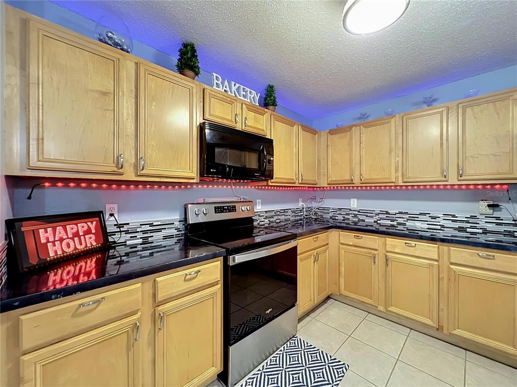 A kitchen features light wood cabinets, black countertops, a tiled backsplash, and under-cabinet lighting — 8307 LAINIE LANE, ORLANDO, FL