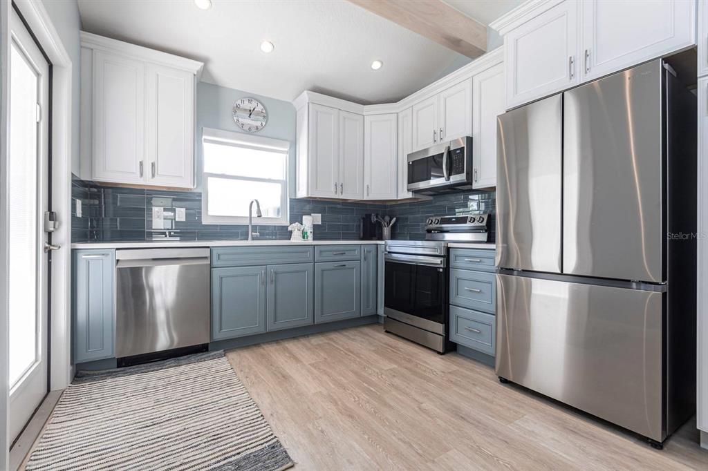 A kitchen features white upper cabinets, blue lower cabinets, stainless steel appliances, and wood flooring — 6020 MIDNIGHT PASS ROAD UNIT 64, SARASOTA, FL