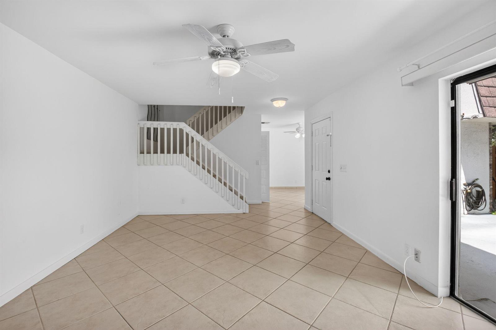 A living area with tile floors, a staircase, a ceiling fan, and a sliding glass door — 7582 Courtyard Run E, Boca Raton FL 33433, BOCA RATON, FL