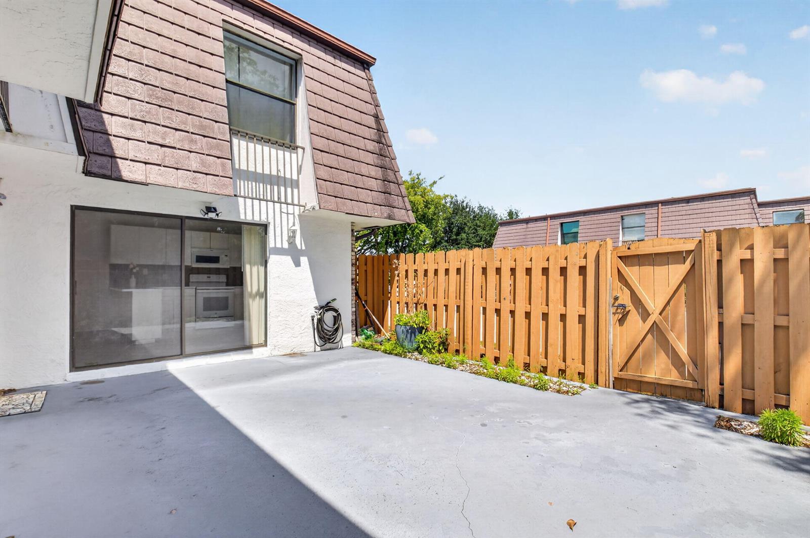 A concrete patio sits outside a sliding glass door next to a wooden privacy fence — 7582 Courtyard Run E, Boca Raton FL 33433, BOCA RATON, FL