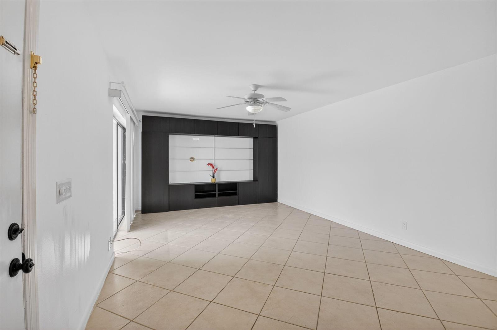 A living room features white walls, tan tile flooring, and a large dark built-in media unit — 7582 Courtyard Run E, Boca Raton FL 33433, BOCA RATON, FL