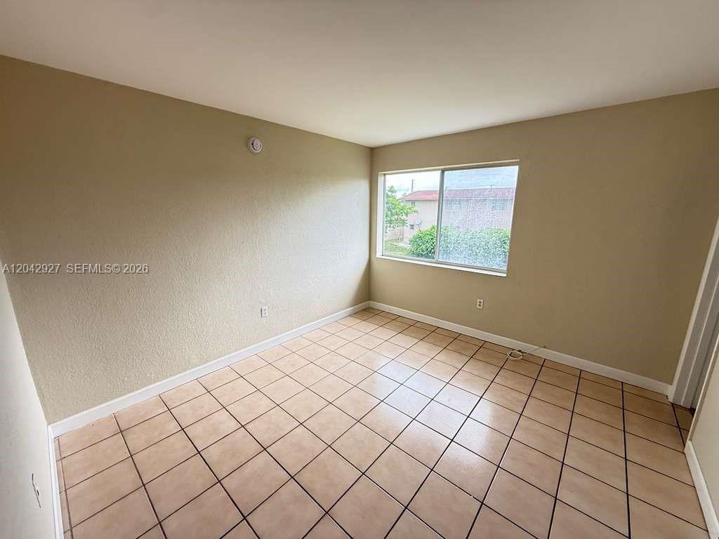 An empty room features beige walls, a window, and light-colored square floor tiles — 1255 W 49th Pl # H202, Hialeah FL 33012, HIALEAH, FL
