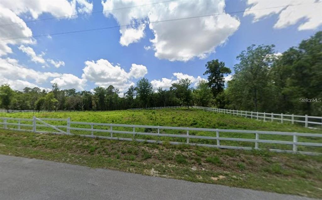 A white fence encloses a grassy, undeveloped lot bordered by trees under a cloudy sky — 7285 NORMAN STREET, WEBSTER, FL