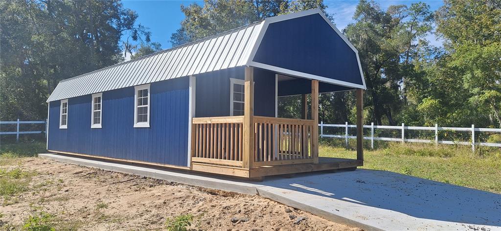 A blue barn-style shed with a metal roof and a front porch sits on concrete — 7285 NORMAN STREET, WEBSTER, FL