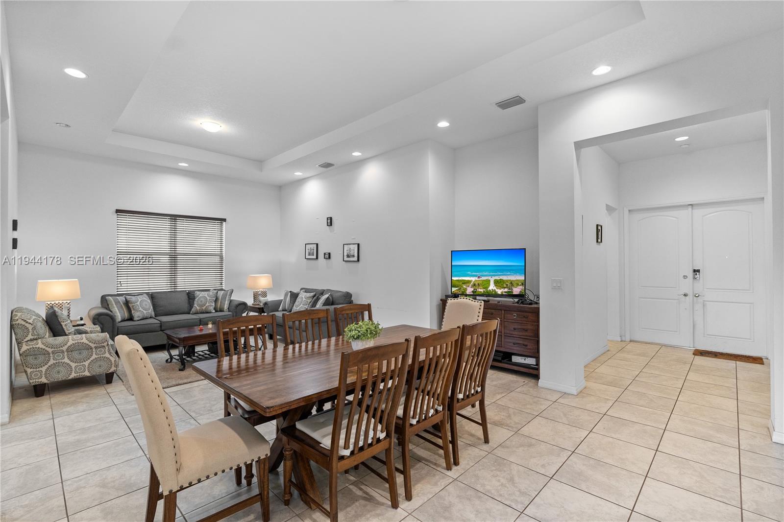 A dining area with a wooden table sits in front of an open-concept living room — 15102 SW 177th Ter, Miami FL 33187, MIAMI, FL