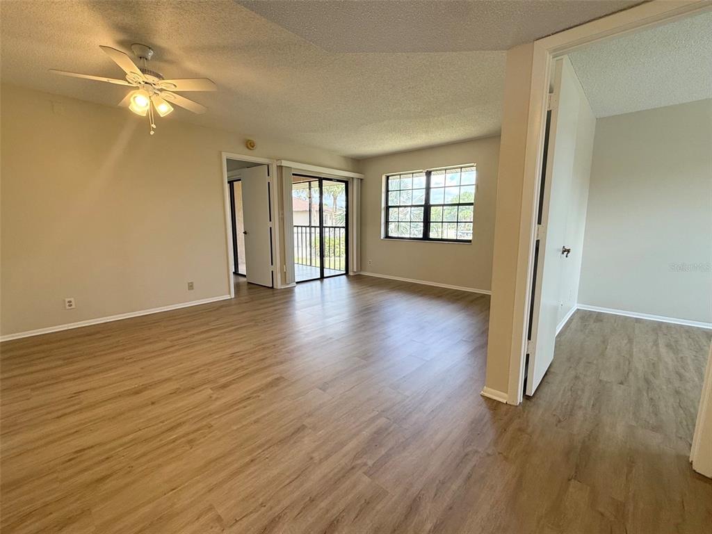 An open living area features light wood-look flooring, a ceiling fan, and a sliding glass door — 19505 QUESADA AVENUE UNIT KK204, PORT CHARLOTTE, FL