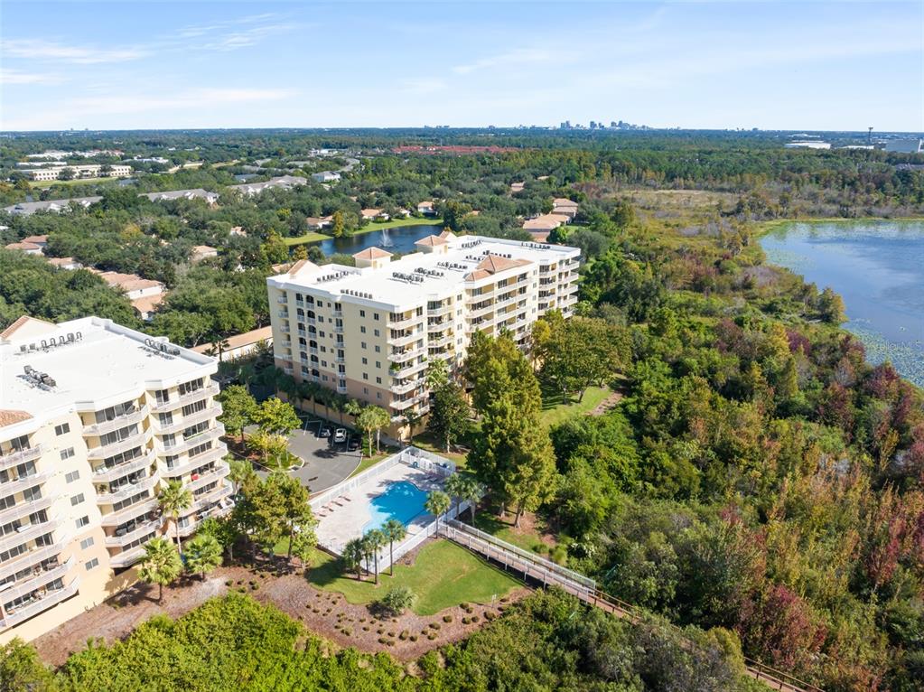 An aerial view shows two multi-story apartment buildings, a swimming pool, and a wooded lakefront — 6312 BUFORD STREET UNIT 704, ORLANDO, FL