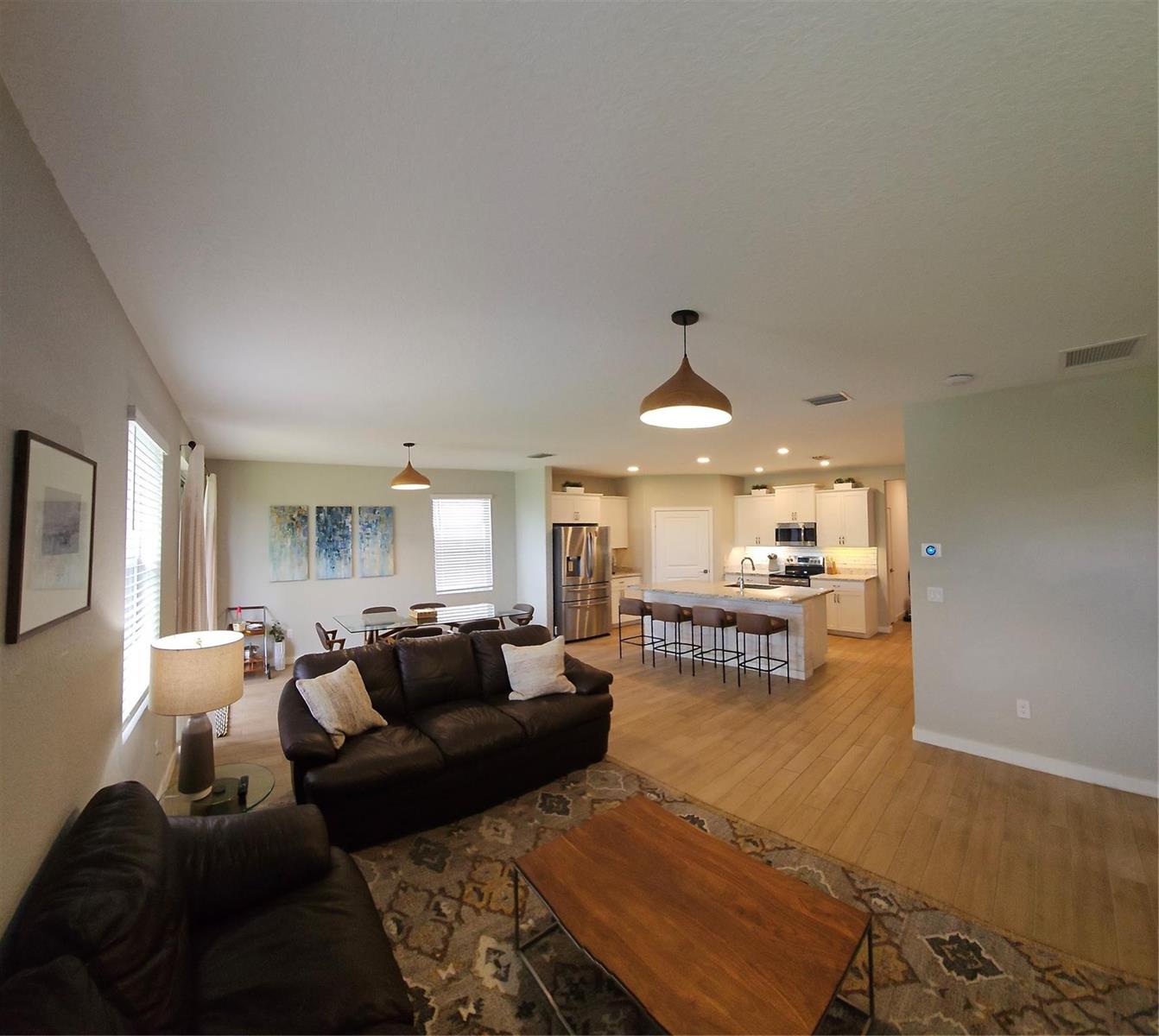 An open-concept living room and kitchen featuring wood-look flooring, a kitchen island, and pendant lighting — 3034 NE Skyview Lane, Jensen Beach FL 34957, JENSEN BEACH, FL