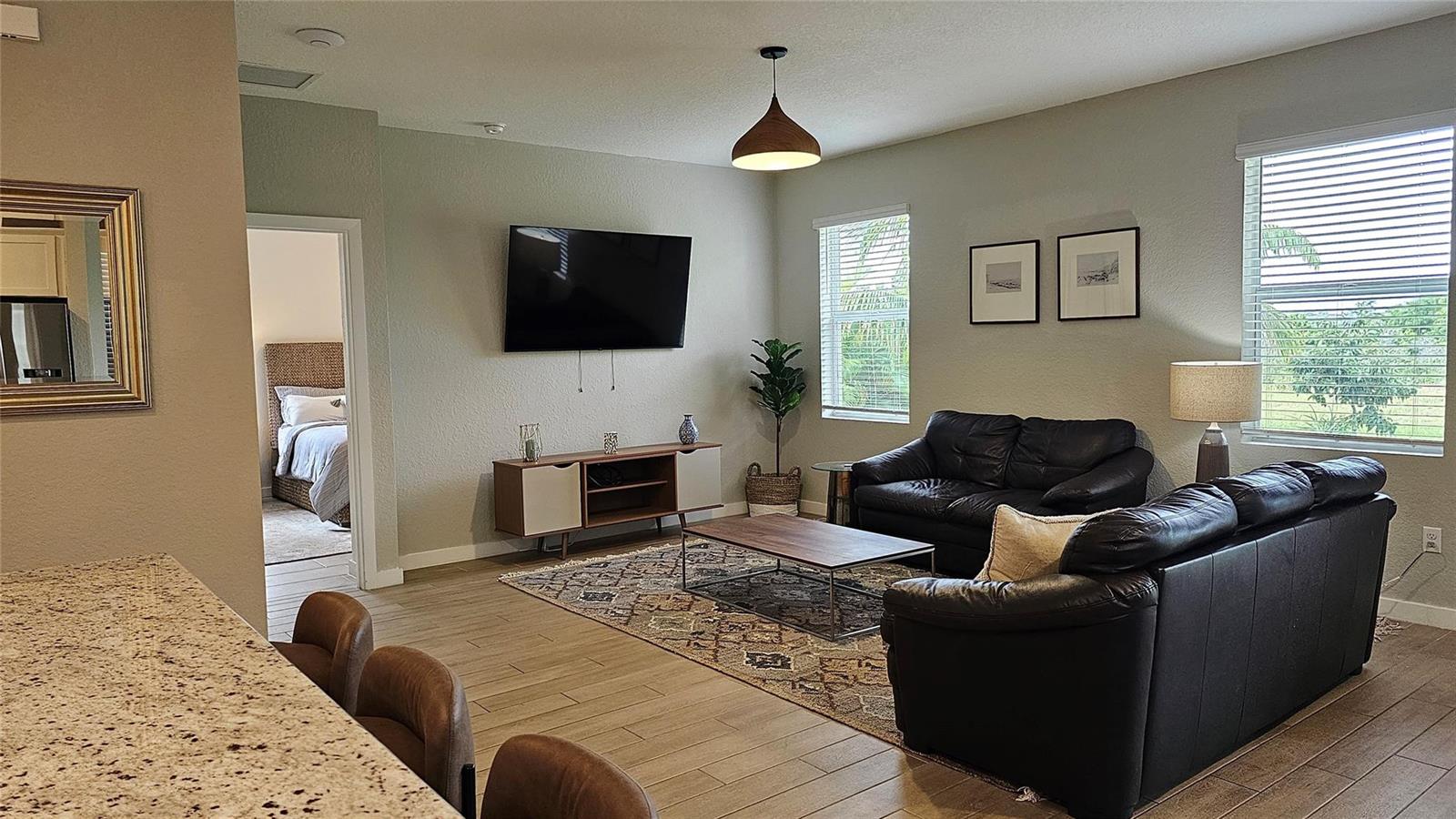 A living room features a black leather sofa, a television, and a patterned area rug — 3034 NE Skyview Lane, Jensen Beach FL 34957, JENSEN BEACH, FL