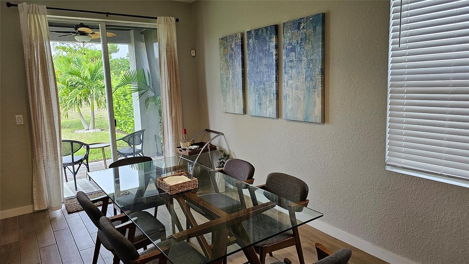 A dining room features a glass-topped table, six chairs, abstract wall art, and sliding doors — 3034 NE Skyview Lane, Jensen Beach FL 34957, JENSEN BEACH, FL