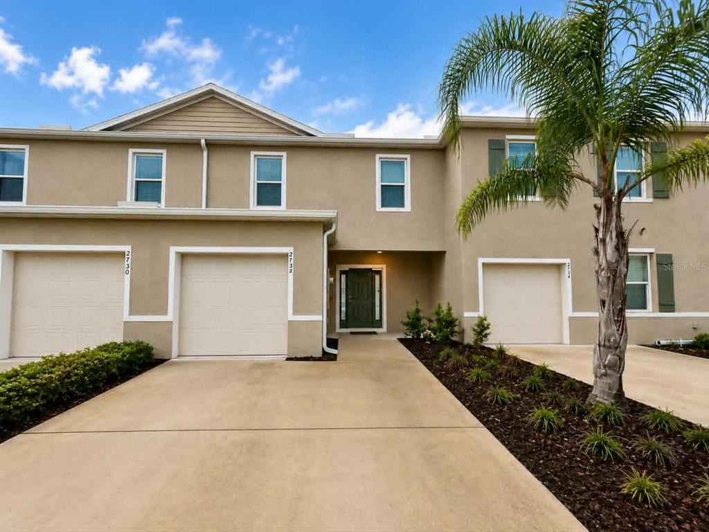 A multi-unit townhouse exterior features beige stucco walls, three garage doors, and a palm tree — 2732 SILVER CANOE DRIVE, EDGEWATER, FL