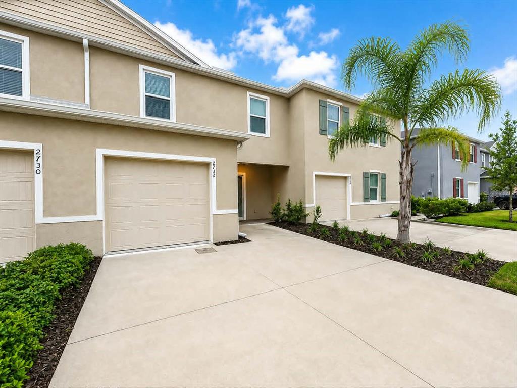 A two-story townhouse exterior features beige stucco walls, two garage doors, and a palm tree — 2732 SILVER CANOE DRIVE, EDGEWATER, FL