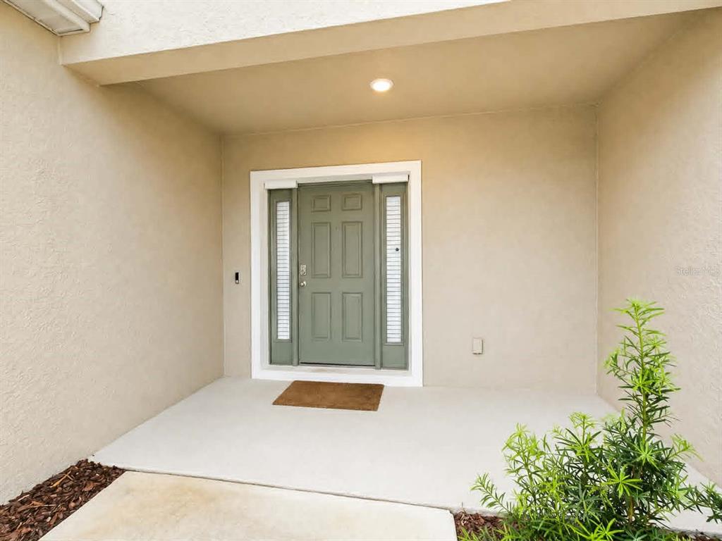 A covered entryway features a sage green front door with sidelights and a concrete porch — 2732 SILVER CANOE DRIVE, EDGEWATER, FL