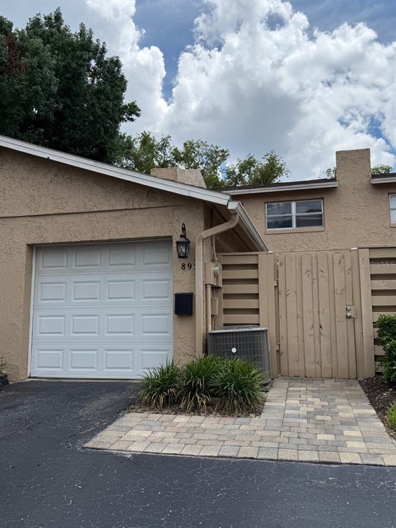 A tan stucco house exterior features a garage, a wooden privacy fence, and a paver walkway — 895 PARK LAKE CIRCLE UNIT 75, MAITLAND, FL