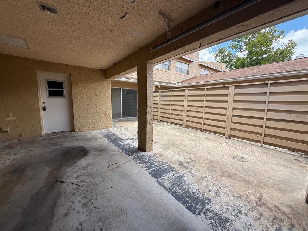 A covered concrete patio area features a white door, a sliding glass door, and horizontal fencing — 895 PARK LAKE CIRCLE UNIT 75, MAITLAND, FL