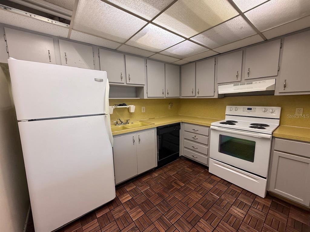 A kitchen with gray cabinets, white appliances, yellow countertops, and a brown tiled floor — 895 PARK LAKE CIRCLE UNIT 75, MAITLAND, FL
