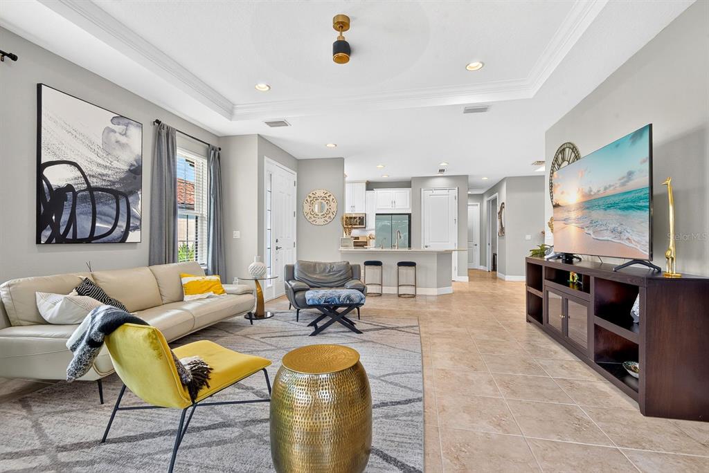 A living room with a beige sofa, yellow accent chair, and television opens to a kitchen — 5319 TALIAFERRO COURT, PALMETTO, FL