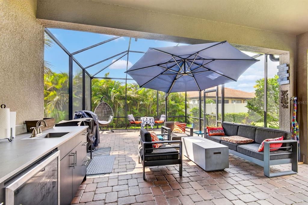 A covered outdoor patio features a kitchen area, lounge seating, and a large blue umbrella — 5319 TALIAFERRO COURT, PALMETTO, FL