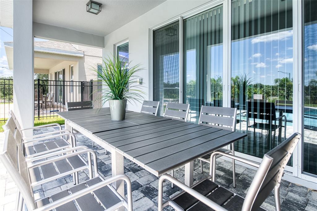 A covered patio features a dining set, a grill, and a view of a pool — 7763 WESTLAND DRIVE, KISSIMMEE, FL