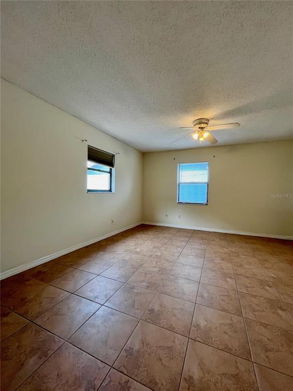 An empty room features beige walls, a ceiling fan, and brown square floor tiles — 6659 WESTMONT DRIVE, ORLANDO, FL