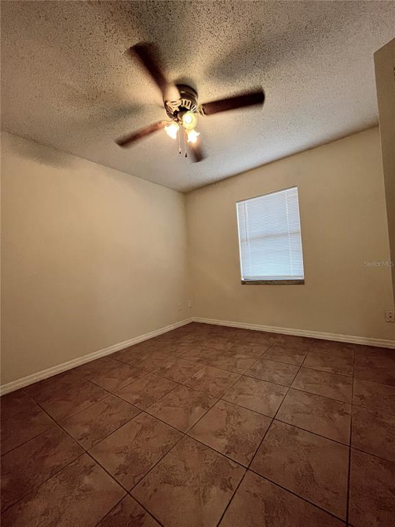An empty room with beige walls, a ceiling fan, and brown tiled flooring — 6659 WESTMONT DRIVE, ORLANDO, FL