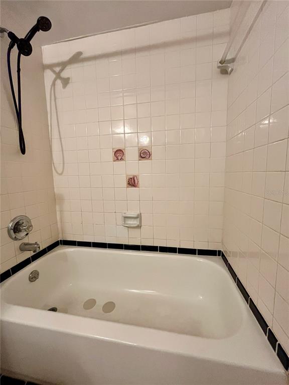 A white tiled bathtub and shower surround with a handheld shower head and decorative accents — 6659 WESTMONT DRIVE, ORLANDO, FL