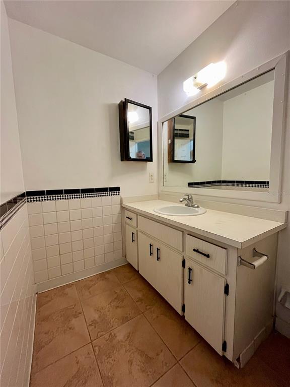 A bathroom features a white vanity with a sink, a large mirror, and tiled walls — 6659 WESTMONT DRIVE, ORLANDO, FL