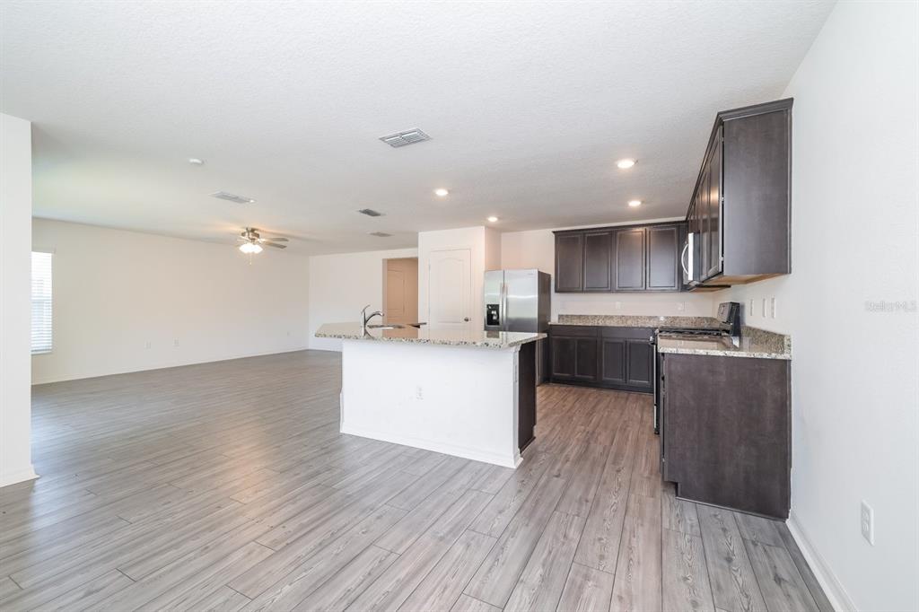 An open-concept kitchen features dark wood cabinets, granite countertops, and light gray wood-look flooring — 465 KENSINGTON VIEW DRIVE, WINTER HAVEN, FL