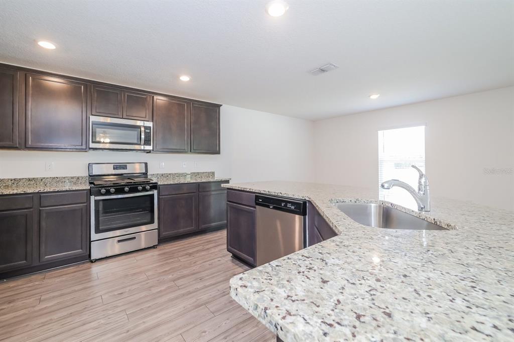 A kitchen with dark wood cabinets, granite countertops, stainless steel appliances, and wood-look flooring — 465 KENSINGTON VIEW DRIVE, WINTER HAVEN, FL