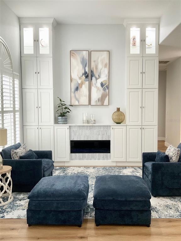 A living room features a fireplace flanked by white built-in cabinets and two navy armchairs — 8027 BELSHIRE DRIVE, ORLANDO, FL