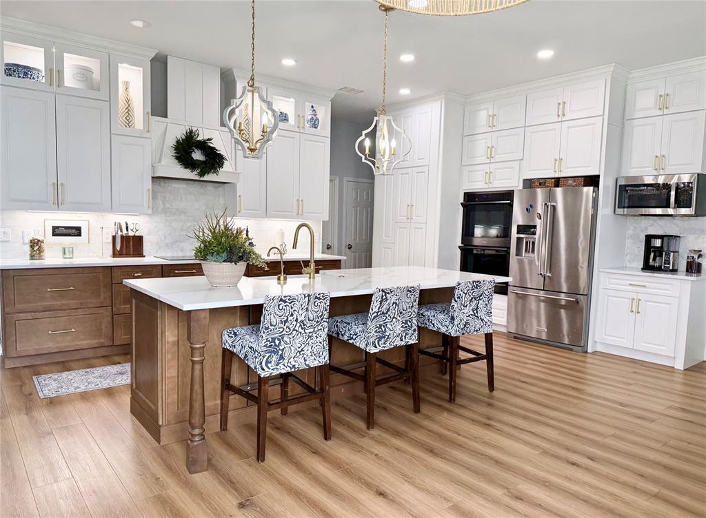 A kitchen features white and wood cabinetry, a large island with barstools, and stainless appliances — 8027 BELSHIRE DRIVE, ORLANDO, FL