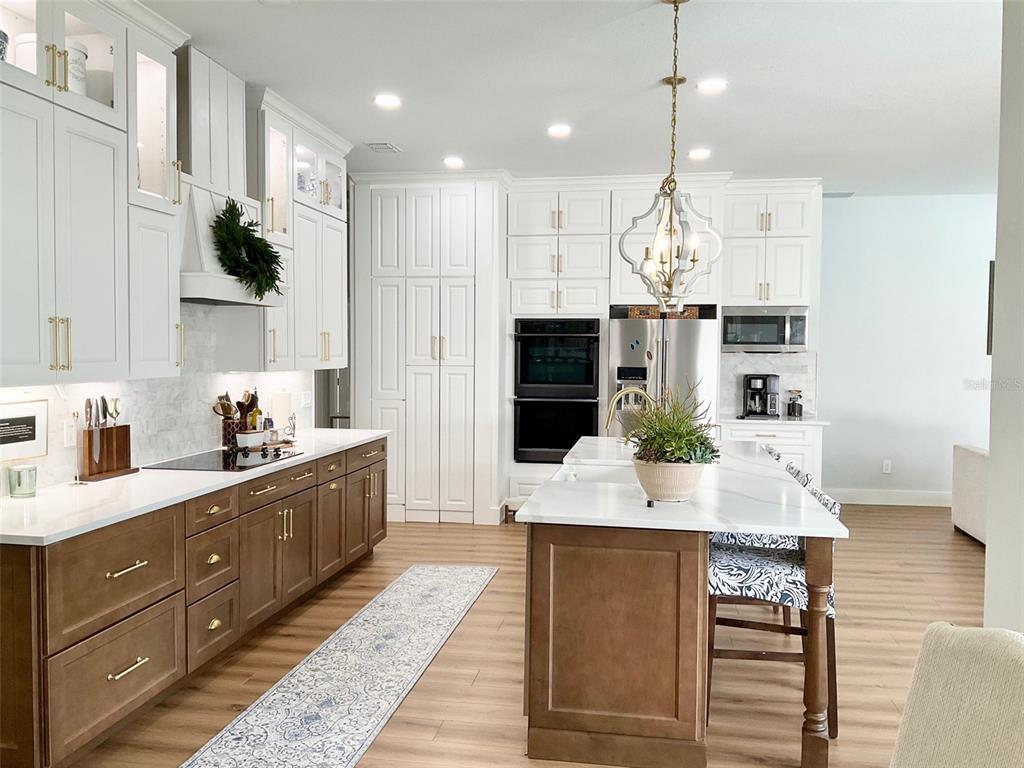 A kitchen features white upper cabinets, wood lower cabinets, a central island, and stainless appliances — 8027 BELSHIRE DRIVE, ORLANDO, FL