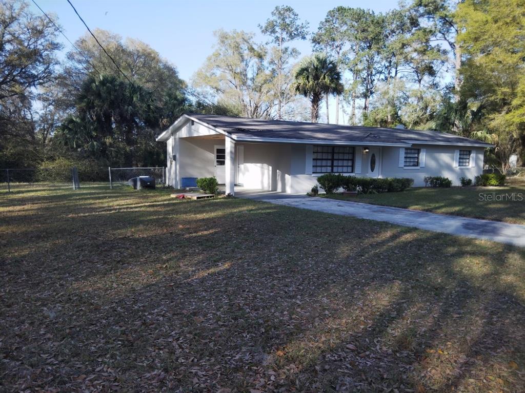 A single-story house with a carport and a large front yard under a clear sky — 11031 NE 145TH STREET, FORT MC COY, FL