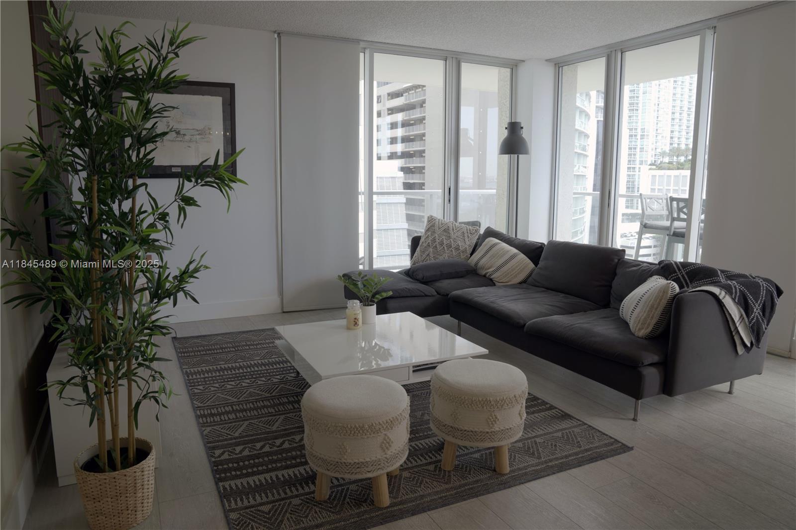 A modern living room features a dark sectional sofa, white coffee table, and floor-to-ceiling windows — 1155 Brickell Bay Dr # 902, Miami FL 33131, MIAMI, FL