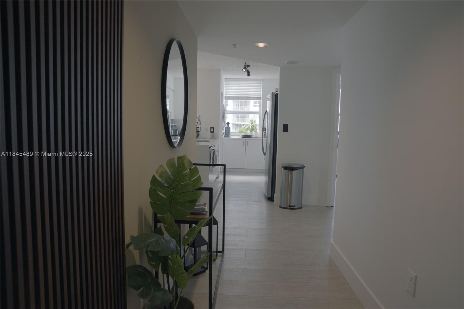 A hallway with light wood flooring leads to a kitchen featuring white cabinets and appliances — 1155 Brickell Bay Dr # 902, Miami FL 33131, MIAMI, FL