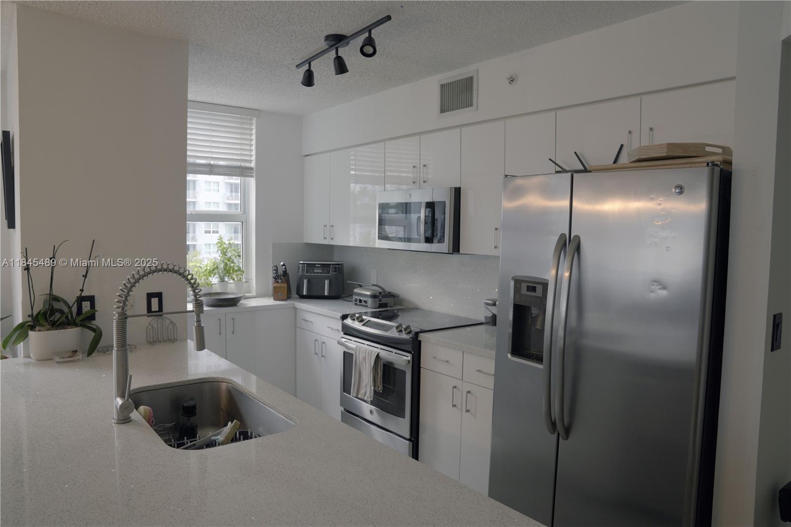 A modern kitchen features white cabinets, stainless steel appliances, and a quartz countertop island — 1155 Brickell Bay Dr # 902, Miami FL 33131, MIAMI, FL