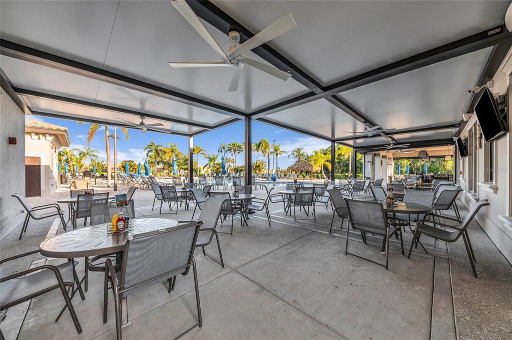 An outdoor covered patio features multiple dining tables and chairs overlooking a swimming pool area — 204 RIVER ENCLAVE COURT, BRADENTON, FL