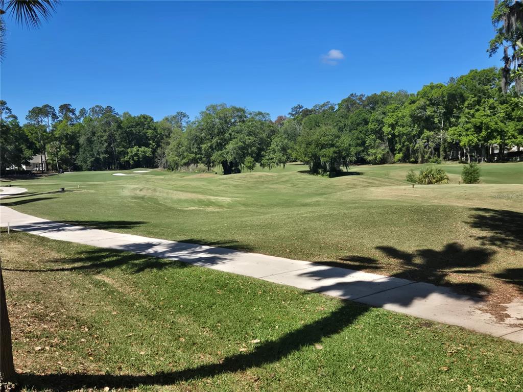 A paved cart path winds through a grassy golf course fairway lined with mature trees — 9123 SW 47TH PLACE, GAINESVILLE, FL
